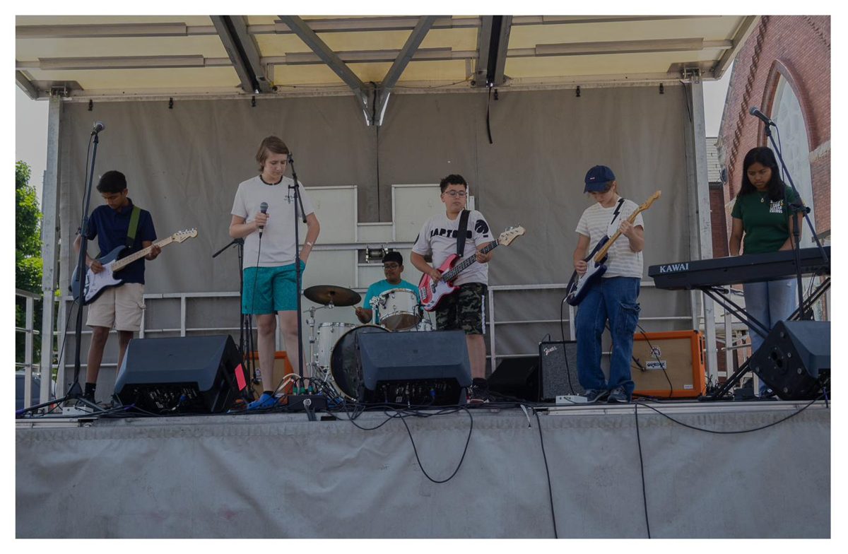An Academy of Music rock band performing on an outdoor stage in Milton
